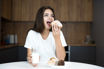 beautiful young woman feeling hungry biting croissant and drinking kefir for breakfast in the...