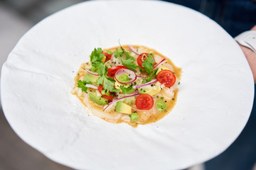 The waiter holds in his hands Tartar from scallop with avocado, cherry tomatoes, radishes and onion. Dish in the restaurant from raw seafood.