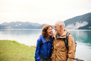 A senior pensioner couple walking by lake in nature, talking.