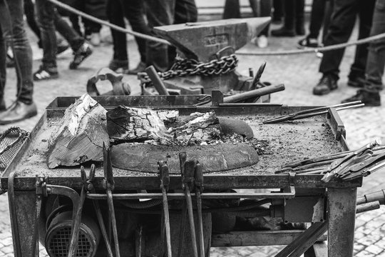 Forge workshop at street fair. Old blacksmith tools on the medieval fair. Anvil, hammer, fire, chain. Forge fire at summer medieval fair. Black and white image