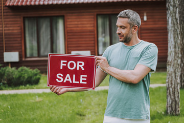 Handsome man holding for sale card outdoors
