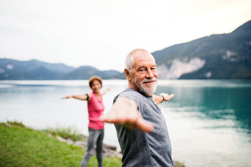 Senior pensioner couple by lake in nature, doing exercise.