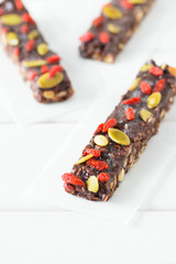 Vegan chocolate bars with granola, goji berries, nuts, pumpkin and chia seeds. Homemade snack. Super energy bars on a white wooden background.