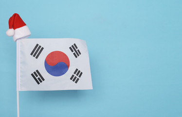 Flag of South korea with little santa claus hat on blue background. New Year winter holiday concept, copy space