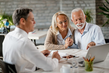 happy senior couple using computer while having a meeting with real estate agent.