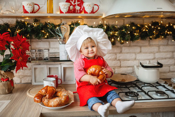 Authentic little girl in a cook hat and apron eats a bun