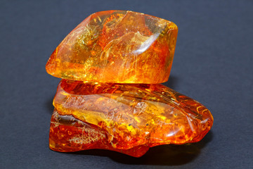 Amber. Two yellow-red polished pieces of natural amber on a blue background. Inclusions in fossil resin. Baltic digging. Sun stone. Color. Natural mineral as a material for jewelers. Crystal