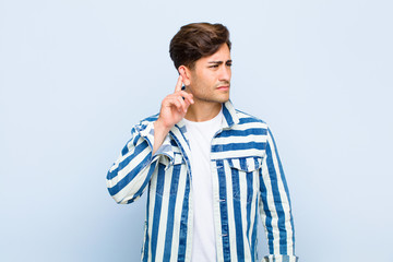 young handsome man looking serious and curious, listening, trying to hear a secret conversation or...