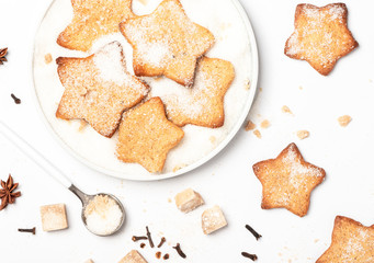 Christmas homemade gingerbread cookie sprinkled with sugar in a plate and spices on a white background, top view. Traditional Christmas sweet pastries.