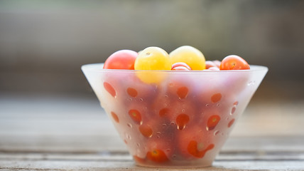 Different sorts of tomatoes served on a white bowl on a wooden background in a blur.