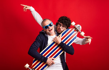 Young man and senior father with longboard in a studio on red background.