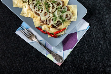 Beshbarmak is a national Tatar dish - square pasta with boiled meat and onions. On a black...