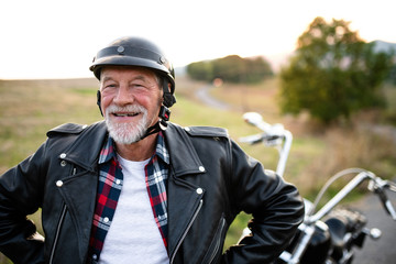 A cheerful senior man traveller with motorbike in countryside, standing.