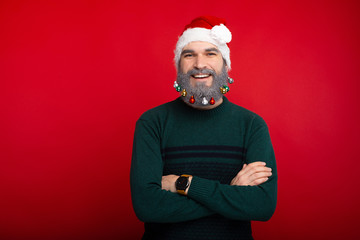 Portrait of Cheerful man with decorated white beard and wearing santa claus hat with crossed arms looking confident at the camera