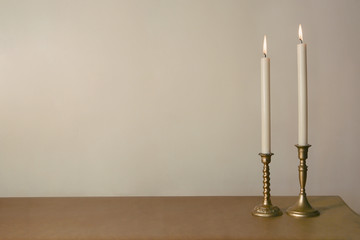 Two candles burning in vintage candlesticks on table against empty wall. . - Powered by Adobe