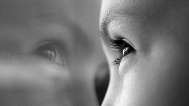 Portrait of a child at the window, eyes very close with a reflection in the glass, black and white