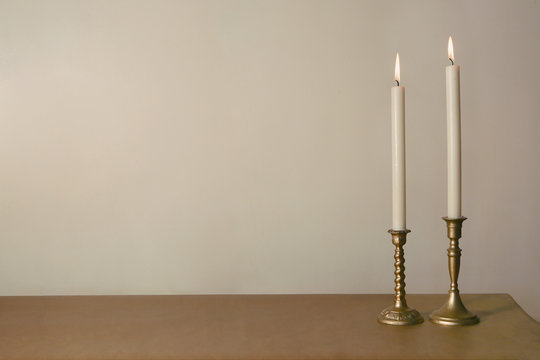 Two candles burning in vintage candlesticks on table against empty wall. .