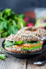 Bagels with cream cheese avocado, fish, arugula and radish on old wooden table. Healthy breakfast food.
