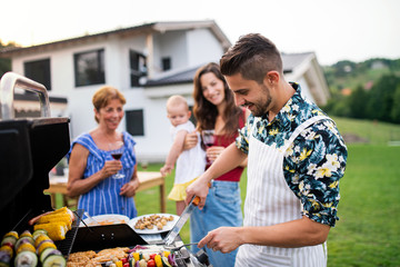 Portrait of multigeneration family outdoors on garden barbecue, grilling.