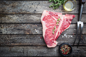 Raw T-bone Steak with fresh herbs and oil on dark wooden background, top view
