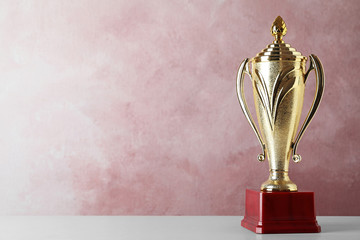 Golden trophy cup on table against pink background. Space for text