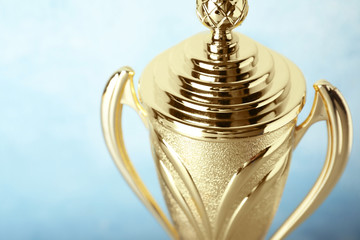 Shiny golden trophy cup on blue background, closeup