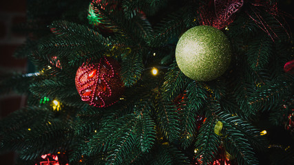 Obraz na płótnie Canvas New Year's red and green shiny balls hanging on a fir branch. Lights and garlands. Christmas and happy new year concept, winter holiday light decoration. Wallpaper.