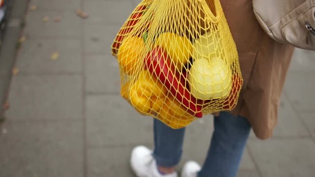 Young woman carries purchases from the grocery store. In the string bag are red and yellow peppers. Eco Packaging, Zero Waste Concept