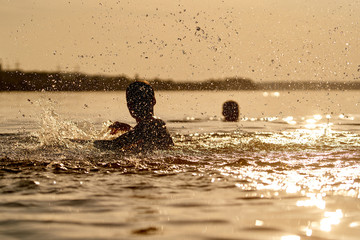 Obraz premium Kid playing in water. Splashes round the boy in river. Beautiful sunset. Summer holidays and childhood concept. Closeup.