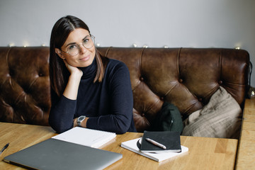 Young business woman sitting at table and taking notes in notebook.On table is laptop, smartphone...