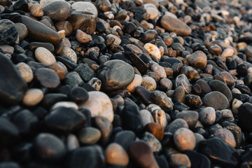 Small stones by the sea with bokeh effect. Blurred decorative background, place for text. Summer wallpaper, sunny sunset light