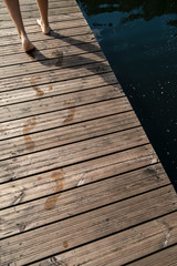Fototapeta premium Wet footprints left by women's feet on a wooden pier. Swimming in the lake on a summer day.