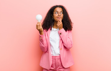 young black pretty woman with a light bulb having an idea against pink wall background