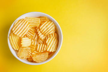 corrugated potato chips in a white plate on a beautiful yellow background. free blank space for text on the right.