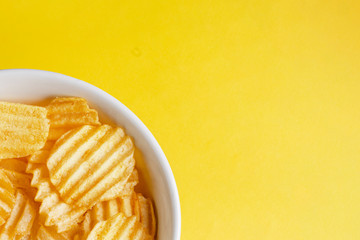 corrugated potato chips in a white plate on a beautiful yellow background. part of the plate large. free blank space for text on the right.