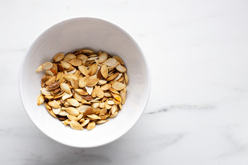 roast Pumpkin seeds in white bowl on marble background with copy space