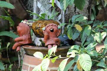 Two clay doll girls sitting on the edge of the tree pot.