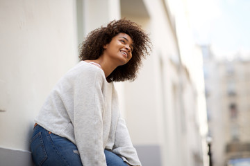 happy young african american woman leaning against wall outside and looking away