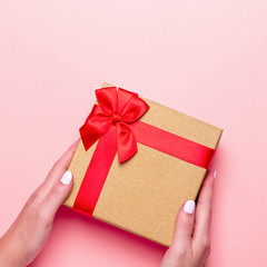 Woman manicured hands holding red and golden wrapped present or gift box on pastel pink background, copy space, top view, flat lay. Background for Valentine's Day, Mother's Day.