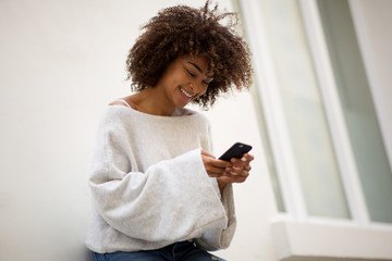 smiling african american woman looking at mobile phone outside