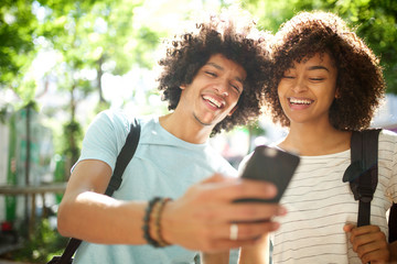 happy young african american couple standing outside looking at cellphone