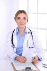 Young woman doctor at work while filling up medication history records in hospital office. Physician controls exam results. Medicine and healthcare concept