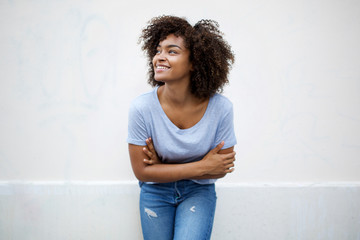 happy young african american woman smiling with arms crossed and looking away by white background