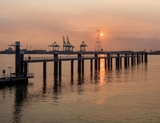 Fototapeta na wymiar Pier in river Scheldt with container terminal on the background at sunset, Port of Antwerp, Belgium.