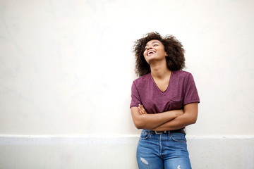 cool african american girl laughing with arms crossed by white wall