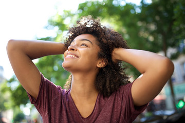smiling african american girl with hands in curly hair looking away