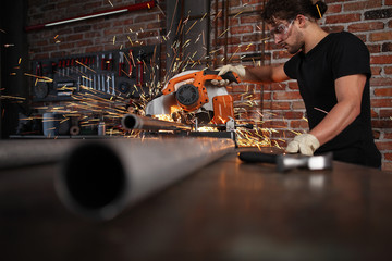 man work in home workshop garage with miter saw, goggles and construction gloves, sawing metal pipe makes sparks, diy and craft concept