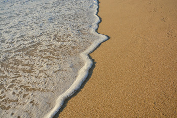Wave of the sea entering the sand of the beach forming foam, contrast of white and beige. Macro photography