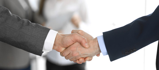 Business people shaking hands while standing with colleagues after meeting or negotiation, close-up. Group of unknown businessmen and women in modern office. Teamwork, partnership and handshake