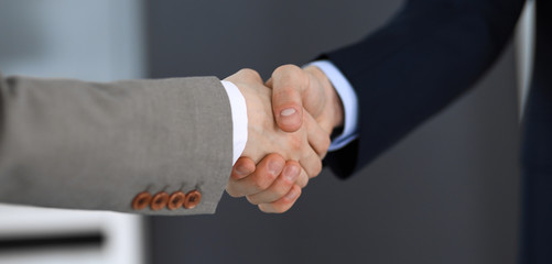 Obraz premium Business people shaking hands while standing with colleagues after meeting or negotiation, close-up. Group of unknown businessmen and women in modern office. Teamwork, partnership and handshake